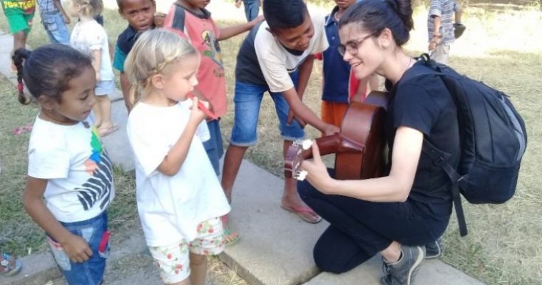 Voluntária se ajoelha para tocar guitarra com crianças